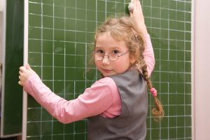 The schoolgirl washes a blackboard with a rag in a classroom